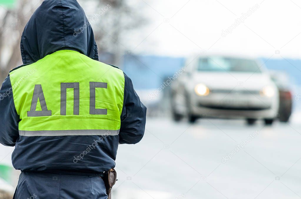 Russian police patrol Inspectorate regulate traffic on city street. Inspector of traffic policein yellow vest jacket with a Russian inscription on the back of the uniform jacket 