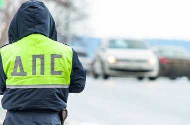 Russian police patrol Inspectorate regulate traffic on city street. Inspector of traffic policein yellow vest jacket with a Russian inscription on the back of the uniform jacket 