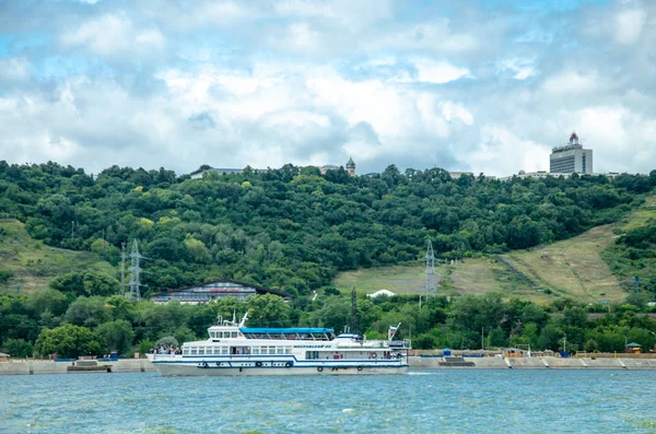 Ulyanovsk, russland - 28. Juli 2019: Ausflugsschiff vor dem Hintergrund der hohen Wolgaküste und der Aussicht auf ulyanovsk. Blick von der Wolga. — Stockfoto