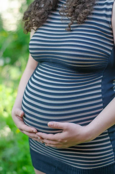 照片上是一个穿着条纹衣服、双手放在肚子上的怀孕女孩 — 图库照片
