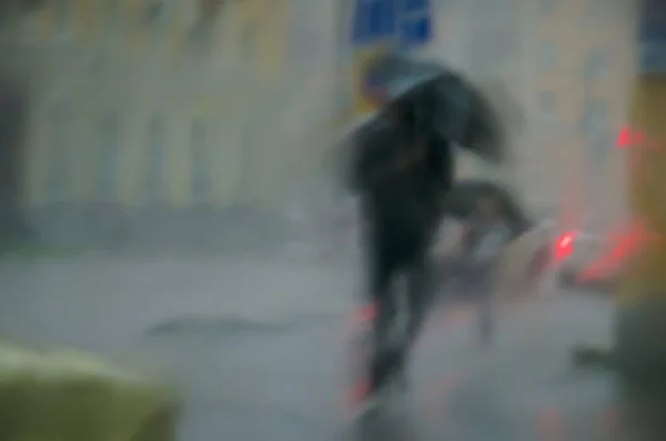 Blurred background on the theme of bad weather in the city. Blurred silhouette of a passer-by with an umbrella against the background of a downpour in the city. Space for text.