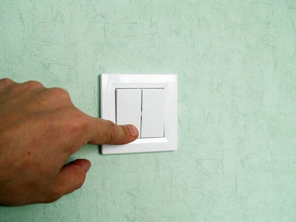 hand turns off the light on the switch located on the wall