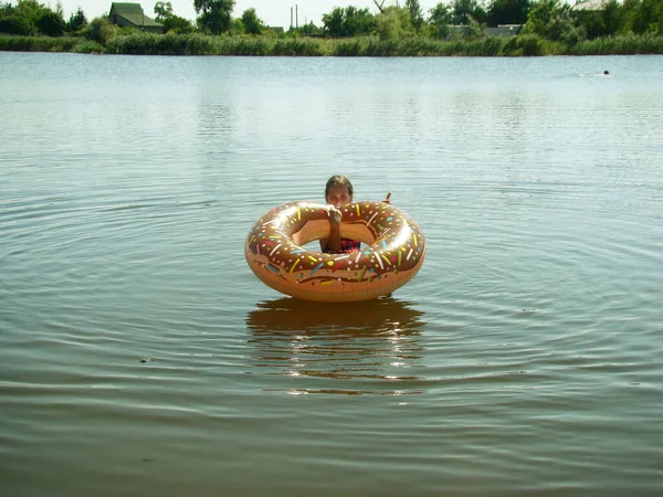 子供はドーナツの形をしたインフレータブルサークルで川を泳いでいます — ストック写真
