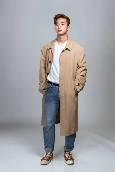 A studio portrait of an East Asian man posing in a coat
