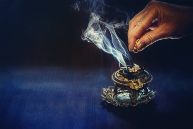 Kadın elinde tütsü, siyah arka planda tütsü dumanı.