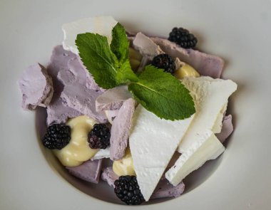 Görüntüyü böğürtlen ve nane ile beyaz ve blackcurrant beze beyaz plaka üzerinde bırakır