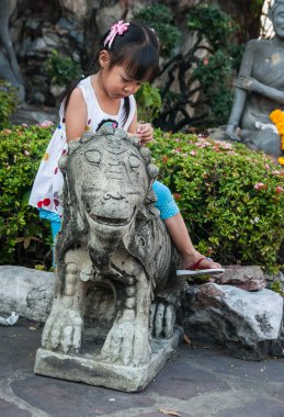 Bangkok, Tayland - 01 Ocak 2011: Bangkok, Tayland için Tapınağı avluda taş aslan ile oynarken küçük Taylandlı kız