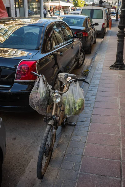 Ποδήλατο με πακέτα με τρόφιμα σταθμευμένο στην οδό μεταξύ αυτοκινήτων σε Άργος — Φωτογραφία Αρχείου