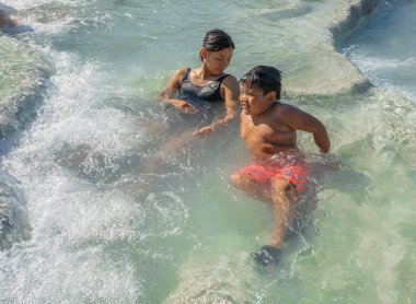 Saturnia, İtalya - 24 Haziran 2020, iki Asyalı çocuk İtalya 'da Toskana, Satürn' de sıcak su havuzlarında şelaleleri ve kaplıcalarla banyo yapıyor.
