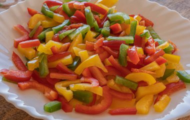 Kırmızı, sarı ve yeşil biber resmi ince dilimlenmiş beyaz bir tabakta, seçici bir odak noktası