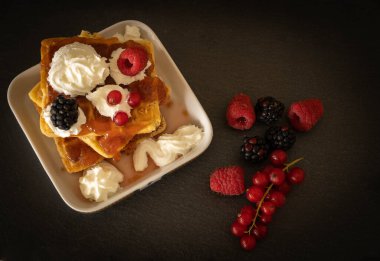 Krem şantili waffle resmi, ahududu, böğürtlen ve koyu arkaplanda kırmızı kaymak.