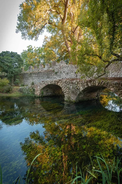 Image of stone bridge with arches and reflection in the water in the Nymph Gardens in the province of Latina in Italy