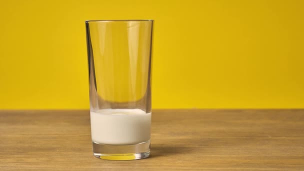 Пачка печенья и стакан молока на деревянном столе с желтым фоном — стоковое видео