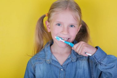 Komik sarışın küçük kız sarı arka plan üzerinde dişlerini fırçalama. Çocuk sağlığı, ağız hijyeni kavramı