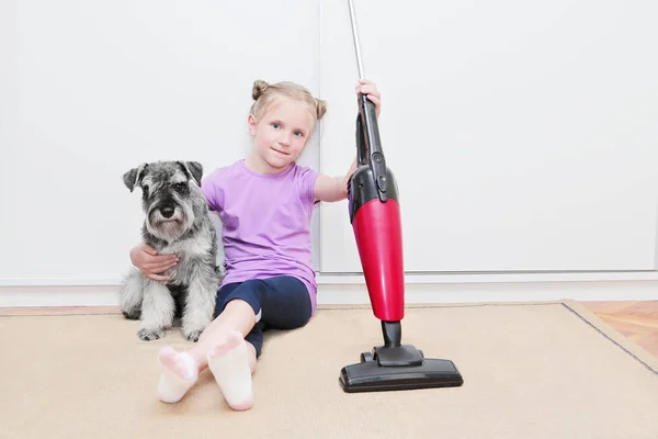 Menina loira bonito e seu cachorro schnauzer sentado em um chão e ter um descanso após a limpeza de um tapete no quarto com um aspirador de pó — Fotografia de Stock