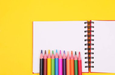 Sarı arka plan üzerinde kopya alanı ile renkli kalem ve defter, okula geri eğitim, satış, alışveriş konsepti.