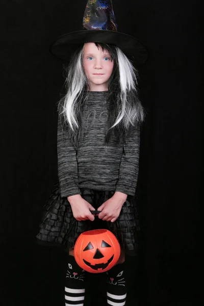 Feliz rindo menina criança no traje de bruxa com frasco de doces de abóbora de Halloween no fundo preto — Fotografia de Stock