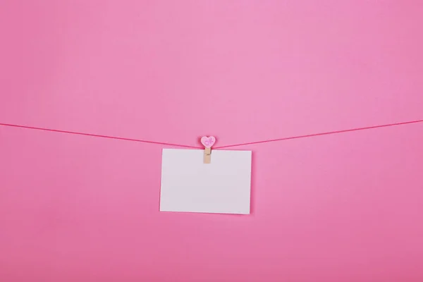 Hojas de papel en blanco sobre una línea de ropa sobre un fondo rosa. Corazones rosados en pinzas de ropa. San Valentín, concepto del Día de la Madre . — Foto de Stock