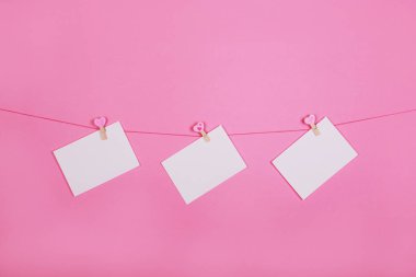 Pembe arka plan üzerindeki bir giysi satırında boş kağıt çarşaflar. Clothespeg'de pembe kalpler. Sevgililer günü, Anneler Günü konsepti.