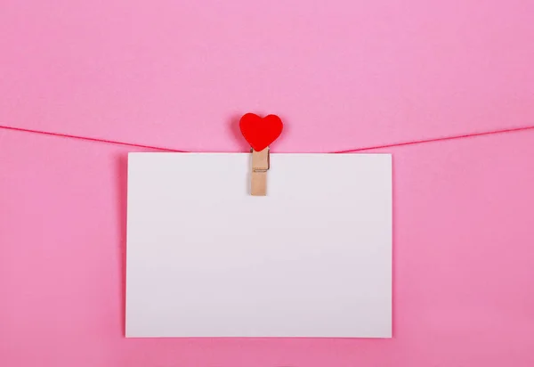 Hojas de papel en blanco sobre una línea de ropa sobre un fondo rosa. Corazones rojos en pinzas de ropa. San Valentín, concepto del Día de la Madre . — Foto de Stock