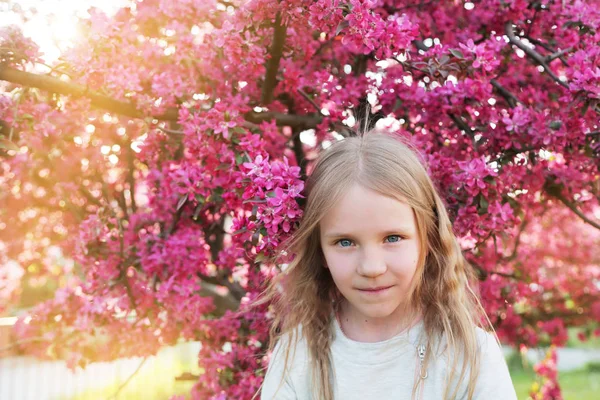 Belle jolie petite fille blonde sentant les fleurs dans le jardin sakura en fleurs . — Photo