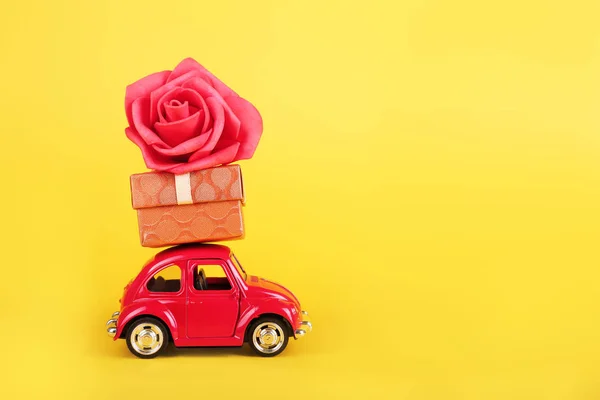 Red retro toy car with red rose flower on yellow background. Flowers, gifts  delivery concept.