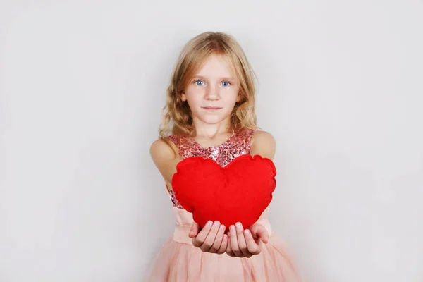 Hermosa chica rubia con el corazón rojo sobre un fondo blanco. Niño con corazón para el día de San Valentín —  Fotos de Stock