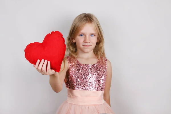 Hermosa chica rubia con el corazón rojo sobre un fondo blanco. Niño con corazón para el día de San Valentín —  Fotos de Stock