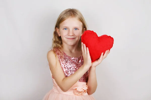 Gyönyörű szőke lány, vörös szívvel, fehér alapon. Gyermek és szív Valentin-napra — Stock Fotó