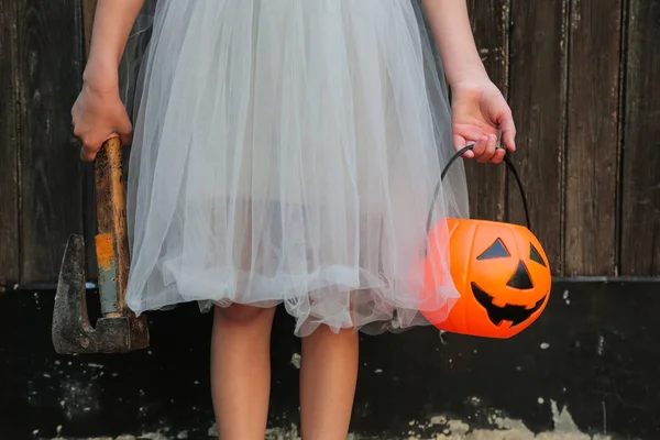 Fille blonde souriante tenant Halloween citrouille Jack O'Lantern et une hache dans les mains sur fond en bois. Fête d'Halloween, concept d'horreur . — Photo