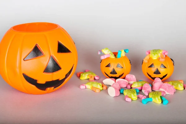 Happy Halloween Trick or Treat jack-o-lantern buckets and a pile of colorful sweets candy on gray background. Пластиковые тыквы для сбора конфет . — стоковое фото