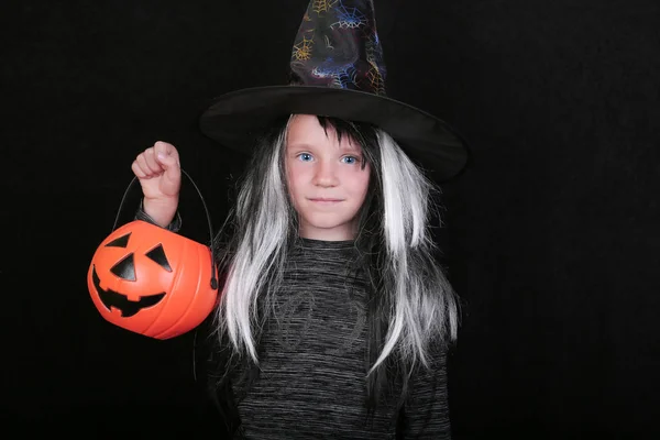 Feliz rindo menina criança no traje de bruxa com frasco de doces de abóbora de Halloween no fundo preto — Fotografia de Stock