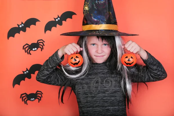 Riant enfant fille avec des citrouilles en costume de sorcière sur Halloween partie. Concept de célébration d'Halloween, fond orange effrayant avec des araignées et des chauves-souris — Photo