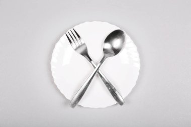 Gri arka plan üzerinde boş beyaz bir tabak üzerinde çatal ve kaşık. 