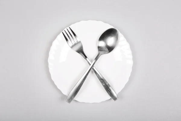 Fourchette et cuillère sur une assiette blanche vide sur fond gris . — Photo