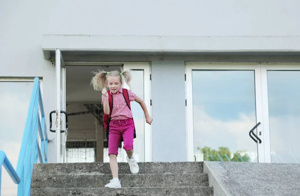 Back to school. Beautiful blond schoolgirl with red backpack running outside the primary school. — Stock Photo, Image