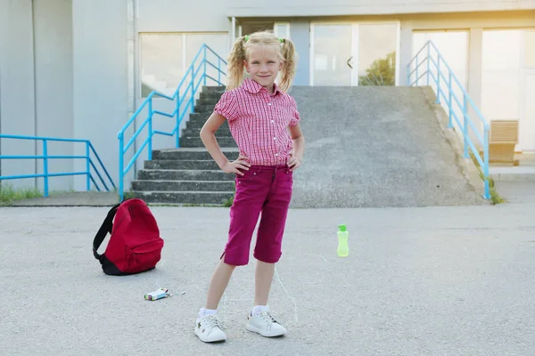 Back to school. Beautiful blond schoolgirl with red backpack play outside the primary school , education concept. — Stock Photo, Image