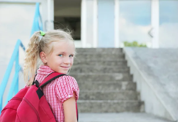 Back to school. Beautiful blond schoolgirl with red backpack outside the primary school from back, education concept. — Stock Photo, Image