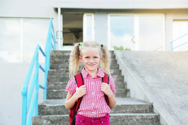 Back to school. Beautiful blond schoolgirl with red backpack and books outside the primary school , education concept. — Stock Photo, Image