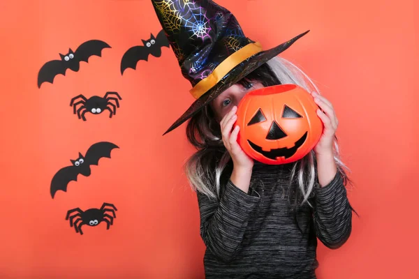 Gargalhada menina com abóboras em traje de bruxa na festa de Halloween. Conceito de celebração de Halloween, fundo assustador laranja com aranhas e morcegos — Fotografia de Stock