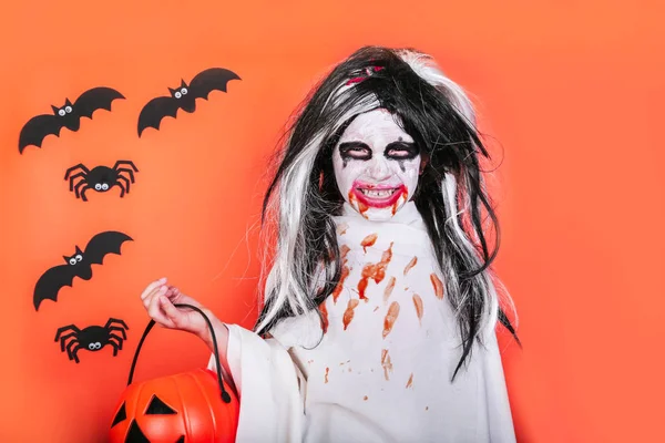 Concepto de horror de Halloween. Linda niña asustadiza en traje de zombi monstruo con calabaza sobre fondo naranja . —  Fotos de Stock