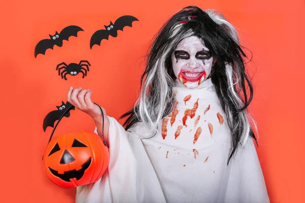 Concepto de horror de Halloween. Linda niña asustadiza en traje de zombi monstruo con calabaza sobre fondo naranja . — Foto de Stock