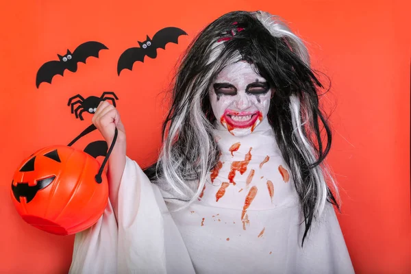 Concepto de horror de Halloween. Linda niña asustadiza en traje de zombi monstruo con calabaza sobre fondo naranja . —  Fotos de Stock