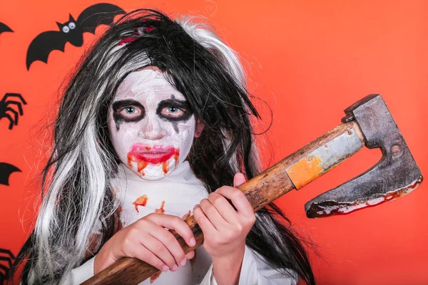 Halloween horror fogalmát. Aranyos kis ijesztő lány szörny zombi jelmez fejsze és vér narancssárga háttér. — Stock Fotó