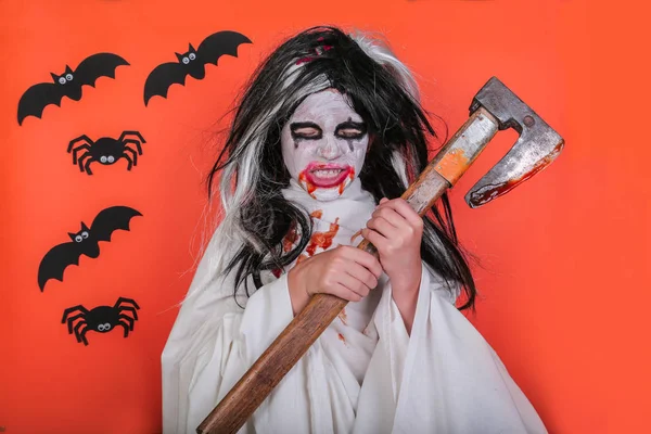 Concepto de horror de Halloween. Linda niña asustadiza en traje de zombi monstruo con hacha y sangre sobre fondo naranja . — Foto de Stock