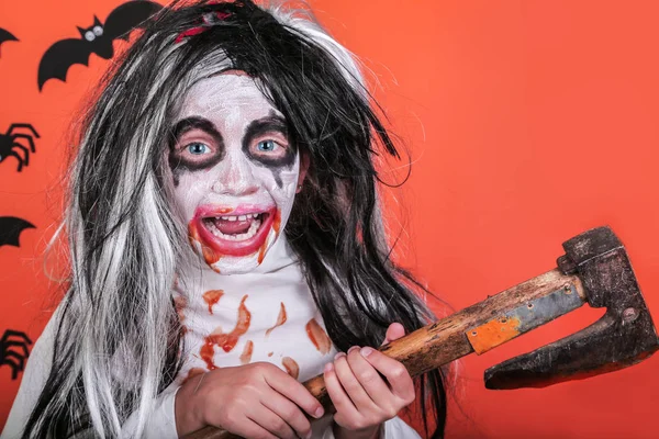 Halloween skräck koncept. Söt liten skrämmande flicka i monster zombie kostym med yxa och blod på Orange bakgrund. — Stockfoto