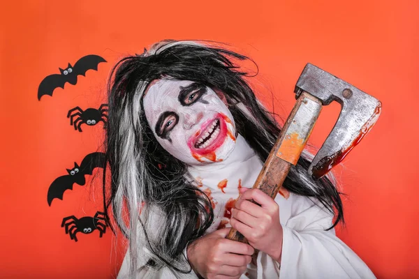 Concepto de horror de Halloween. Linda niña asustadiza en traje de zombi monstruo con hacha y sangre sobre fondo naranja . — Foto de Stock