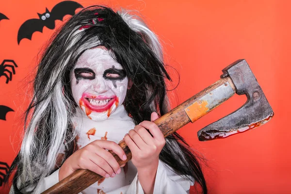 Halloween horror fogalmát. Aranyos kis ijesztő lány szörny zombi jelmez fejsze és vér narancssárga háttér. — Stock Fotó