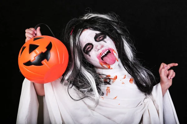 Concepto de horror de Halloween. Linda niña asustadiza en traje de zombi monstruo con calabaza sobre fondo negro . —  Fotos de Stock