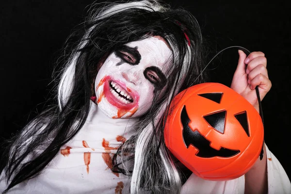 Concepto de horror de Halloween. Linda niña asustadiza en traje de zombi monstruo con calabaza sobre fondo negro . —  Fotos de Stock